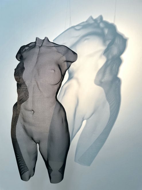 A large shadow appears behind a hanging torso sculpture of a female body - artwork by sculptor David Begbie