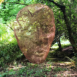 A large wire-mesh head sculpture is suspended in a summer garden.