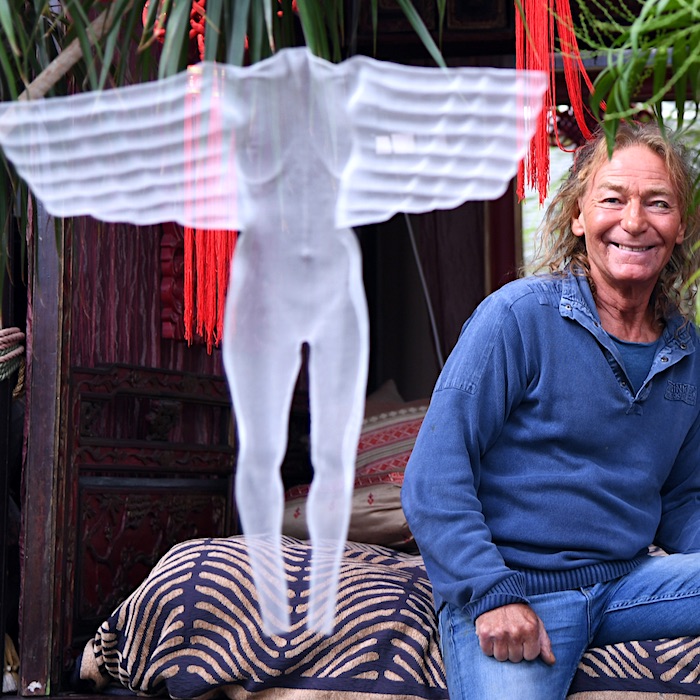 Artist sitting on his indonesian bed with angel sculpture made fro wire fabric