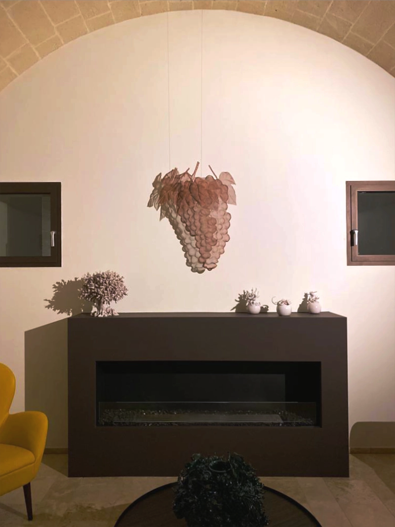 A wallart depicitng a grape made from wired steel is suspended in a winery lobby abouve the fireplace. Artwork commission 2022.
