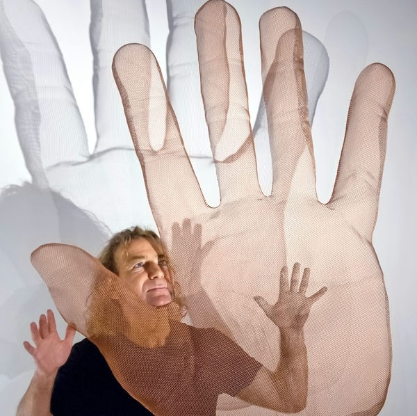 Artist David Begbie stands behind his transparent mesh sculpture of a large hand