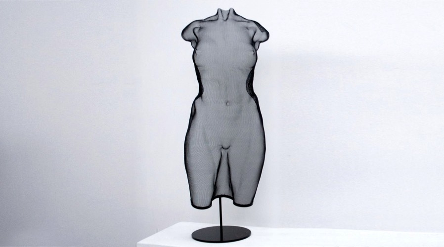A freestanding, female torso made from black painted steel mesh
